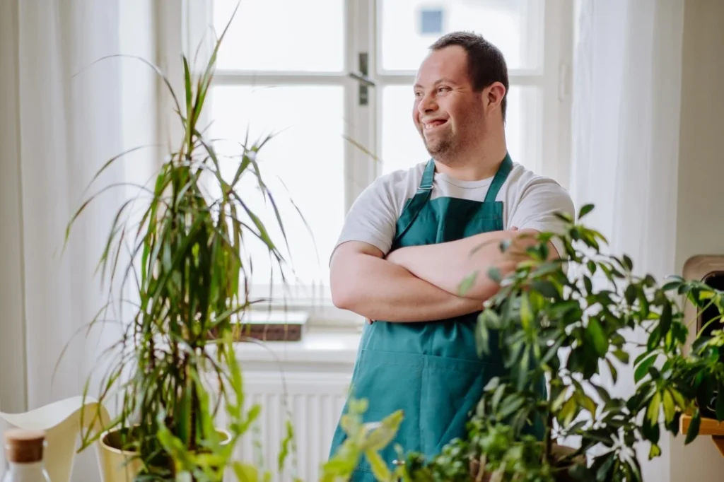 Disabled man with down syndrome smiling wearing apron and surrounded by plants